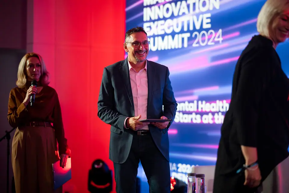 A smiling speaker on the EXS 2024 stage, with the mental health panel title on screen
